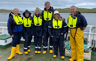 A group of visitors to Scottish Sea Farms pose for a photo aboard a boat.