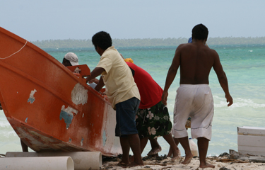 Kiribati fishermen move a boat onto shore.