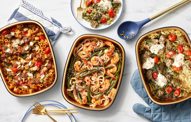 Three Blue Apron ready to cook meals in serving dishes on a table.