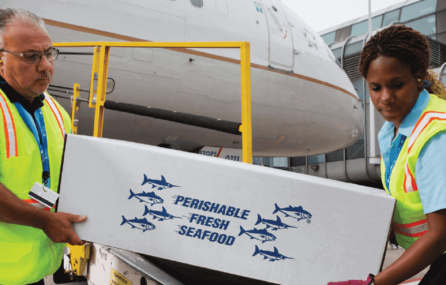 Two airport employees offload a seafood shipment from a plane