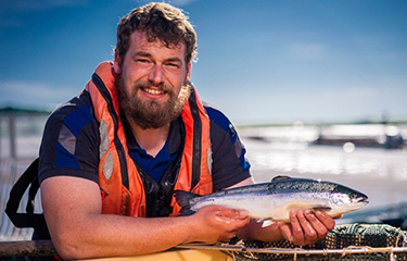 A Scottish salmon farm employee holding up a young salmon.