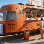 An AI-generated rendering of an orange truck serving shrimp to people on the beach