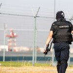 An ICE officer in front of a fence