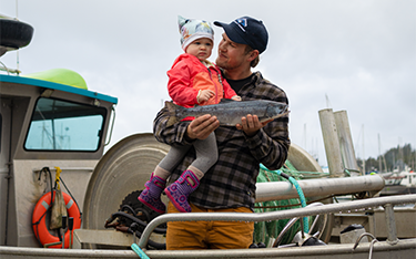 Alaska fisher holds up his toddler and a pink salmon.