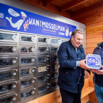Two men show the packaged mussels you can purchase from a new mussel vending machine.