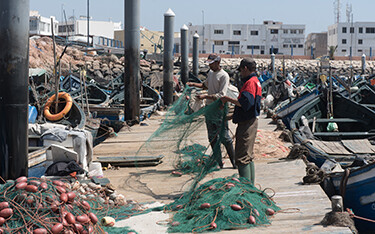 A pair of fishermen maintain nets on a pier in Morocco.