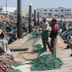 A pair of fishermen maintain nets on a pier in Morocco.