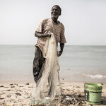 A Senegalese fisherman holding a net stands on the shoreline of Senegal.