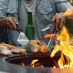 A man grilling cuts of salmon at a fire.