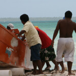 Kiribati fishermen move a boat onto shore.