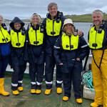 A group of visitors to Scottish Sea Farms pose for a photo aboard a boat.