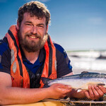 A Scottish salmon farm employee holding up a young salmon.