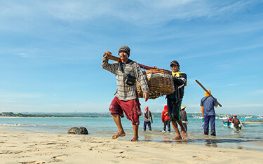 Indonesian fishermen carrying a boat onto shore.