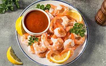 A plate of cooked shrimp with a dipping sauce and lemon slices.