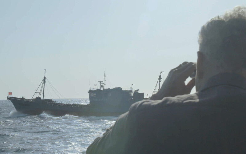 Ian Urbina looking through binoculars at a fishing vessel