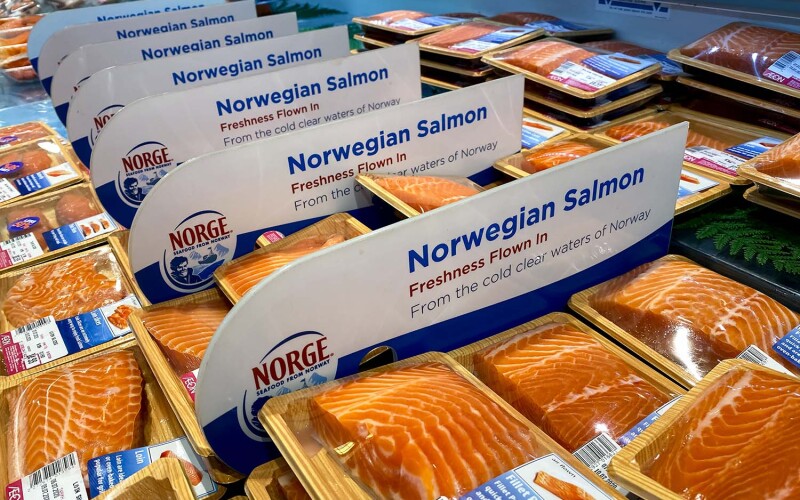 A supermarket display case filled with packaged Norwegian salmon, with a sign that says "Norwegian salmon, freshness flown in"