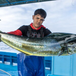 A young Peruvian fisher holding up and looking at a mahi he caught