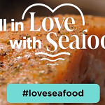 A promotional photo for Seafood Nutrition Partnership's "Fall in Love with Seafood" campaign featuring a seasoned, cooked fish fillet