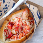 A lobster roll from Luke's Lobster inside Luke's Lobster branded paper packaging.