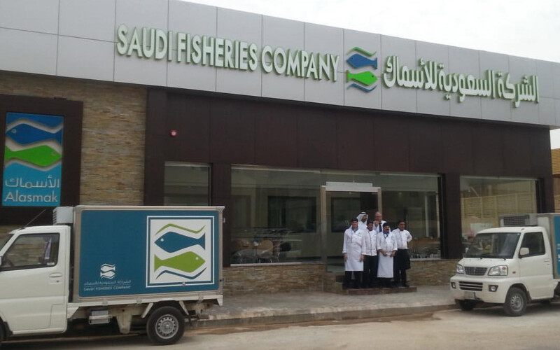 A storefront for Saudi Fisheries Company with small delivery trucks and a group of staff posing for a photo