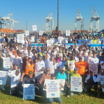 A large group of International Longshoreman's Association members posing with picket signs at a port.