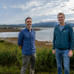 Nordlaks Smolt Operations Director Øivind Skjevling and Executive Director Eirik Welde stand in grass by the ocean shore.