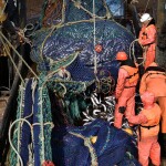 A group of five Russian fishermen in orange gear pulling in a large net full of fish