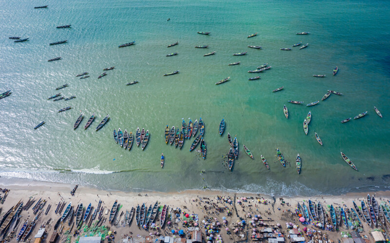 An aerial photo of artisanal fishing boats lined up on the coast of Tanji, a Gambian fishing village