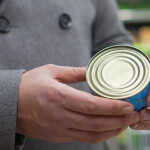 A close-up photo of a man's hands holding a can of seafood