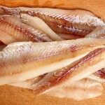 A pile of pollock fillets on a wooden cutting board.