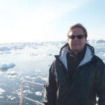 A photo of Sebastian Belle on board a boat, with a calm sea covered in ice in the background