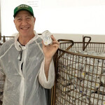 Bela Brand Seafood Founder Joshua Scherz holding tinned sardines next to large containers of tinned sardines
