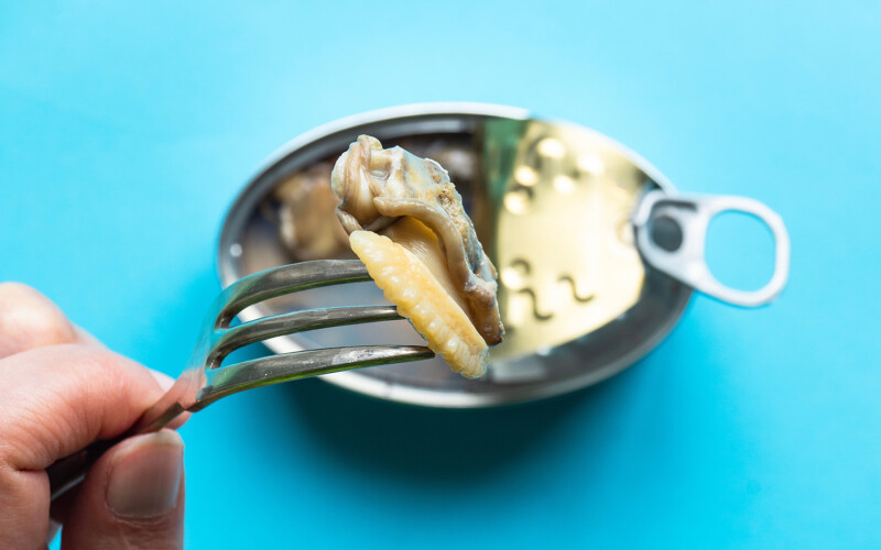 A canned clam product on a fork, with the can in the background