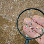 A person looking at pieces of plastics through a magnifying glass at the beach