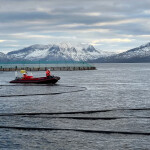 Cermaq Group employees on a boat at a salmon farm with snowy mountains in the background