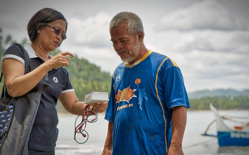 A woman showing a Southeast Asian fisher how to use a piece of monitoring technology