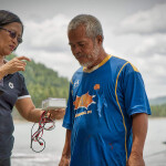A woman showing a Southeast Asian fisher how to use a piece of monitoring technology
