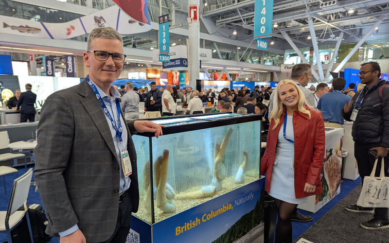 Underwater Harvesters Association Executive Director Grant Dovey and Marketing Manager Katie Lindsey posing near a tank of geoduck at Seafood Expo North America