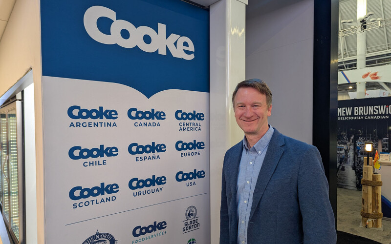 Cooke Vice President of Public Relations Joel Richardson standing next to Cooke logos at its booth at the 2025 Seafood Expo North America