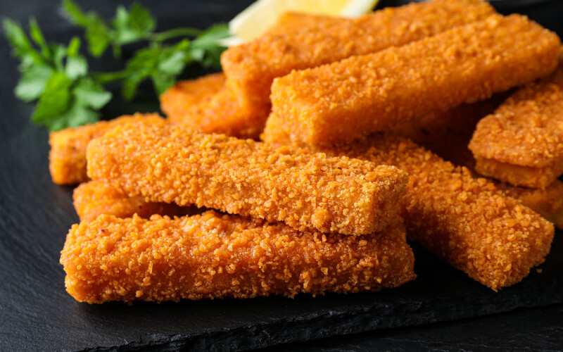 A pile of fish sticks on a black plate with a lemon