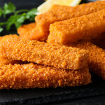 A pile of fish sticks on a black plate with a lemon