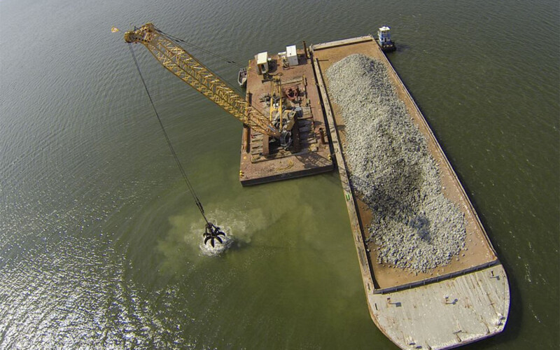 A crane depositing rocks on the ocean floor for oyster reef restoration