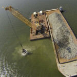 A crane depositing rocks on the ocean floor for oyster reef restoration