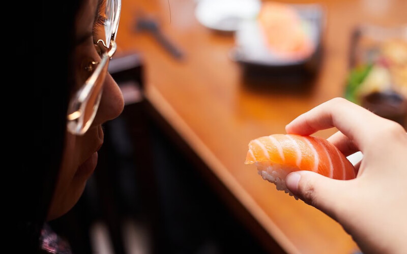 A Japanese woman holding a piece of salmon nigiri