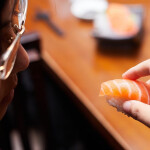 A Japanese woman holding a piece of salmon nigiri