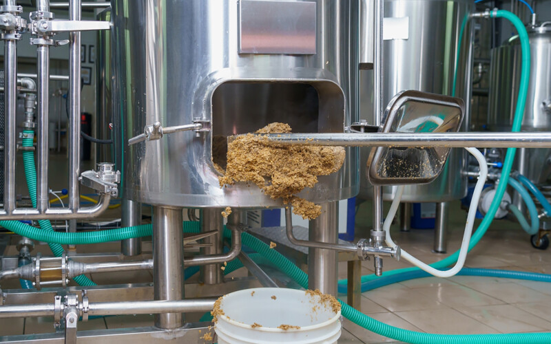 Brewer's spent grain being shoveled out of a stainless steel vat