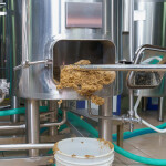 Brewer's spent grain being shoveled out of a stainless steel vat