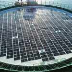 An aerial view of a AKVA-created salmon net pen, covered in solar panels