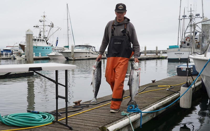 A man walking on a dock holding two salmon
