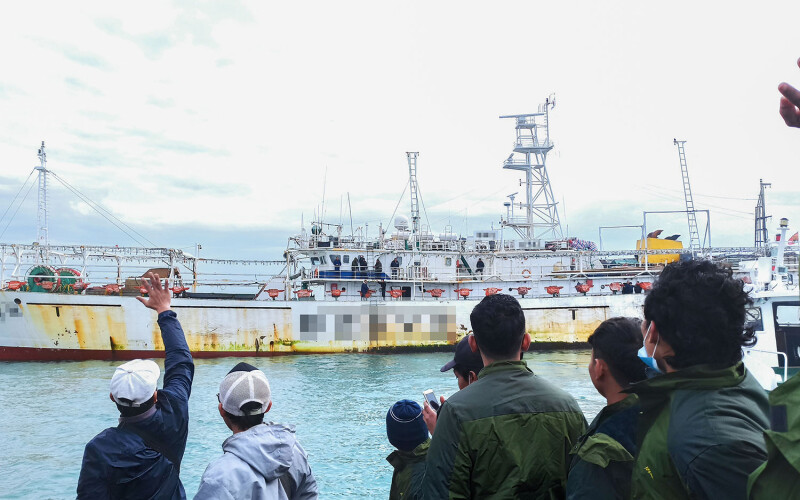 Men on shore wave at a fishing vessel